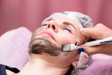 Obraz na płótnie Canvas Applying a cream mask for carbon peeling on the face of an adult woman.