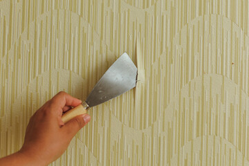 Preparing the wall for painting or sticking new wallpaper. Woman in gloves with a scraper in the...