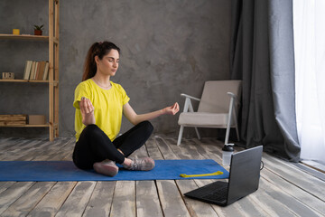 Young woman meditates and listens to music in front of a laptop, girl doing yoga training fitness workout sport exercise