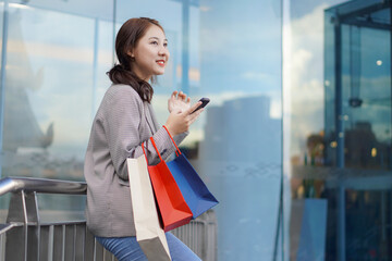 Smiling Asian woman with shopping bags above the floor of a department store in a shopping mall facility. Women's fashion, shopping, lifestyle, happiness, consumption, sales and people concept.