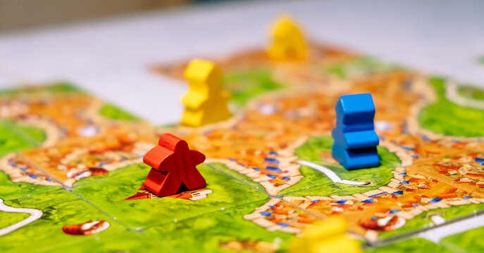 Board game Carcassonne. Party entertainment or family leisure hobby. Play together. Strategic and economic table game. Concept of fun time. Different colors chips. Wooden meeple figures. Close-up