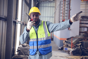 A portrait of technician working or operating in metal factory while radio communication with...