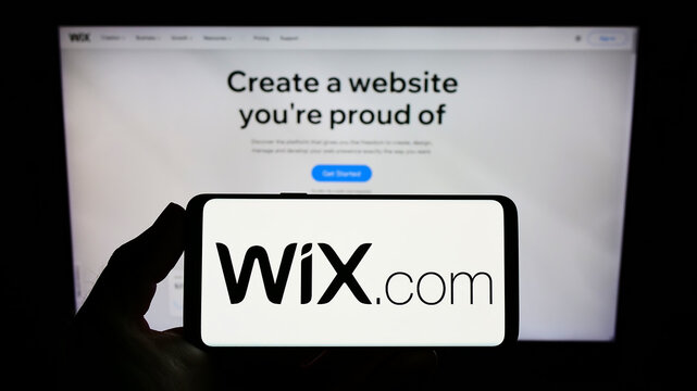 Stuttgart, Germany - 03-01-2022: Person holding smartphone with logo of Israeli software company Wix.com Ltd. on screen in front of website. Focus on phone display.