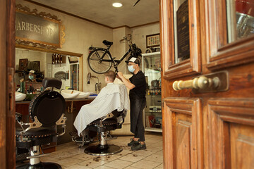 Fototapeta na wymiar Stylish barber makes a fashionable haircut to a young guy. People at work. Small business or services concept. Professional haircut and styling in a barbershop or hairdressing salon