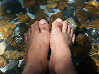 Comfortable holiday Soaked his bare foot in the stream. 
Couple foot dipped in serene lake transparent water with pebbles.