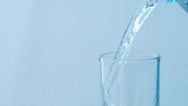 Slow motion of pouring water from the bottle into glass on blue background.