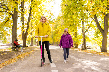 Youg mother walking with her daughter riding a toddler scooter in park.