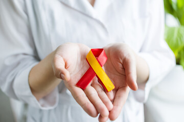 World hepatitis day. Doctor woman holding in her hands red yellow ribbon. Awareness of prevention and treatment viral hepatitis. Liver cancer. World cancer day. banner. close-up - obrazy, fototapety, plakaty