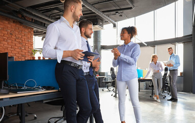 Group of modern business people are talking and smiling while standing in the office hallway