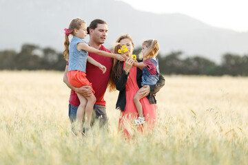 Fototapeta premium Happy family father of mother and two daughters sisters on nature at sunset.Carefree parents having fun with their kids on a field.