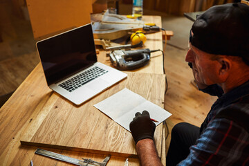 Senior carpenter works on the computer and talks phone with client in the workshop