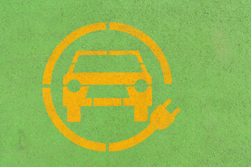 Yellow electric car symbol on green asphalt. Electric vehicle charging parking