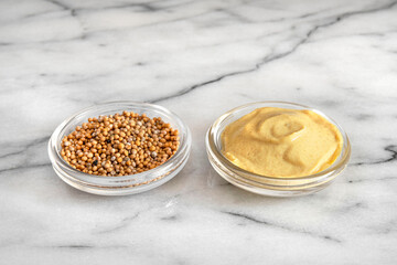 Close-up of mustard seeds and yellow mustard in glass bowls