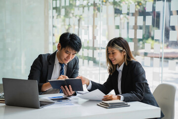 Team of Asian young business people analyzing data using a computer while talking about marketing strategy and planning working in the office