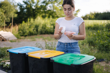 Woman throwing out in recycling bin washed and empty shampoo and deodorant bottles. Female looks at...