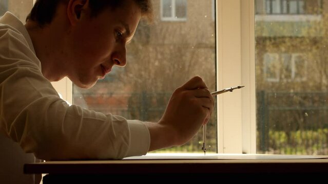 Young mathematician and designer Pavel drawing circle with using a compass, side view. Date of shooting day 30 April 2022 year, MSK time. This video was filmed in Russia.