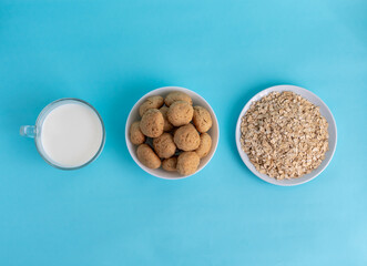 Flatlay oatmeal, oatmeal cookies on a white plate, milk in transparent glass on a blue background, top view, the concept of healthy eating and making cereal or cookies. High-quality photo