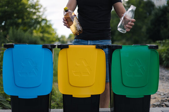 Close up of man hold two different bottle, plastic and glass and thowing into different recycling bins. Close-up of woman stand by blue, yeallow and green bin