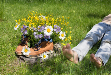 Brown shoes with bouquet of wildflowers in them, resting child lies on grass nearby. flower...