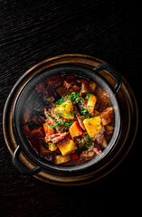 Goulash. Vegetable rague with meat, eggplant, pepper, potato and carrot in black bowl on dark wooden background