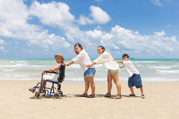 senior woman in a wheelchair with family helping and support on the beach