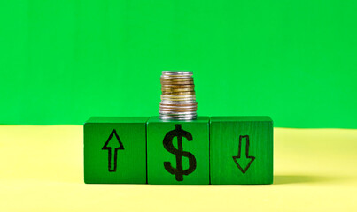 Stack of coins on green cubes with signs of dollar currency and arrows up and down on green background. Inflation concept and market instability. Copy space