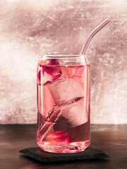 A glass of pink gin and tonic made with rose infused tonic water, on a light pink background