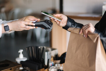 Young woman paying bill through smartphone using NFC technology in a cafe. Female customer paying using contactless technology. Closeup hands of mobile payment at a coffee shop