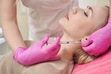 Obraz na płótnie Canvas Pretty Caucasian female with silk skin receiving injection into her ear in salon