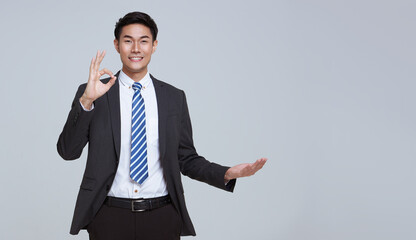 Handsome and friendly face asian businessman smile in formal suit gesture or showing hand ok on...
