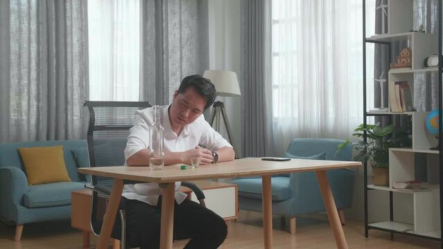 Drunk, Depressed Asian Man With Smartphone On Table Drinking Vodca From The Bottle At Home
