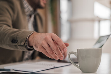 Close-up of professional reaching for coffee cup on desk while working at office