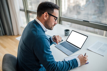 High angle view of serious businessman writing notes while sitting at office desk. White blank...