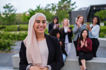 Young woman with hijab smiles applauded by her co-workers