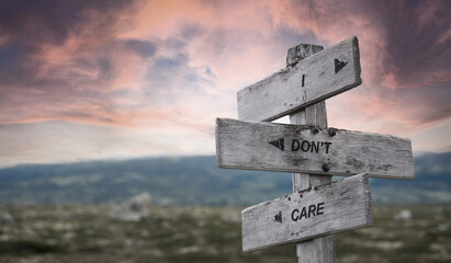 i dont care text quote caption on wooden signpost outdoors in nature with dramatic sunset skies. Panorama crop.
