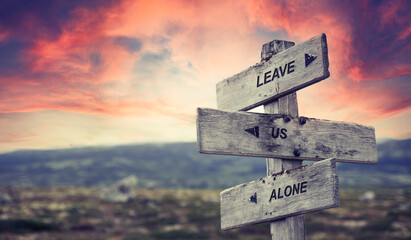leave us alone text quote caption on wooden signpost outdoors in nature with dramatic sunset skies....