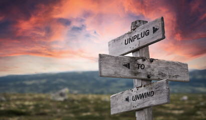 unplug to unwind text quote caption on wooden signpost outdoors in nature with dramatic sunset...