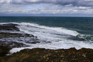 Smooth waves on sea reaching to rocky shore.