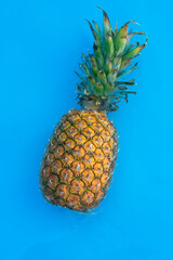 Natural pineapple in a swimming pool with a blue background
