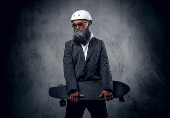 Studio shot of sportive senior man dressed in elegant casual attire holding skateboard.