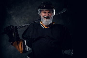 Portrait of happy elderly sportsman dressed in black protective sportswear holding hockey stick.