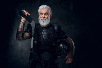Portrait of elderly professional sportsman dressed in protective sportswear holding hockey stick.
