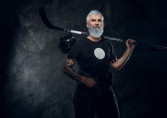 Shot of cool aged hockey player dressed in sportive uniform holding hockey stick.