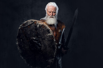 Studio shot of old man knight dressed in chain mail and leather armor holding shield and sword.