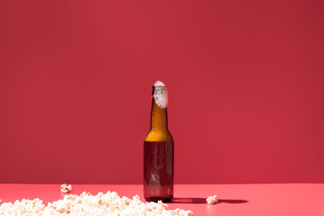 Palomitas de maíz con una botella de cerveza sobre un fondo rojo