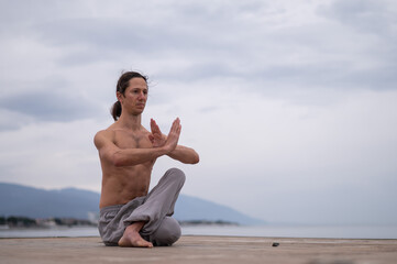 Caucasian man with naked torso practicing wushu on the seashore. 