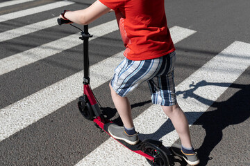 A teenager with a scooter crosses the road at a pedestrian crossing. Road safety © LariBat