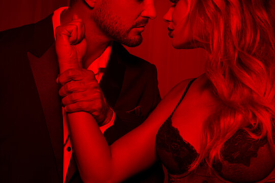 Strong dominant rich man holding blonde lovers hand, passionate couple in red light