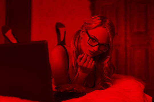 Sexy blonde woman typing on laptop in red light