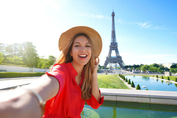 Fashion tourist woman with red dress and hat makes selfie photo with Eiffel Tower on the background in Paris, France. Concept travel. - obrazy, fototapety, plakaty
